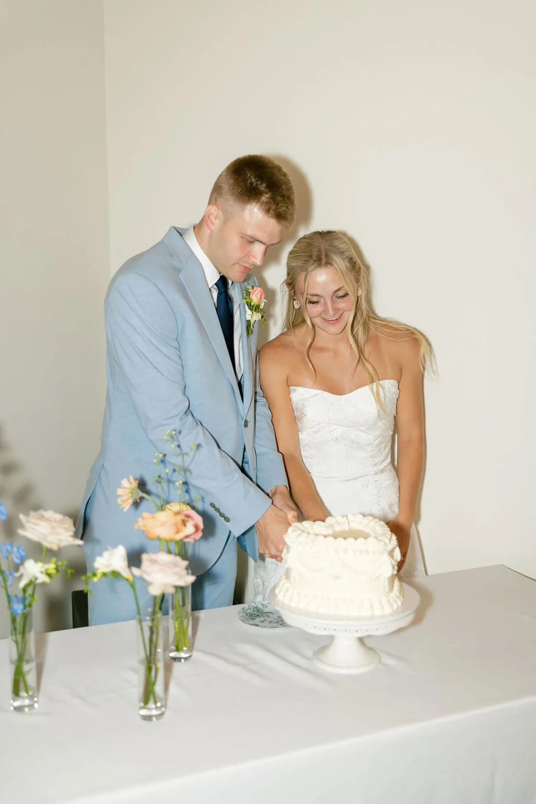 Bride and groom cutting a small white wedding cake with blush and blue florals at Gateley Hill Gardens