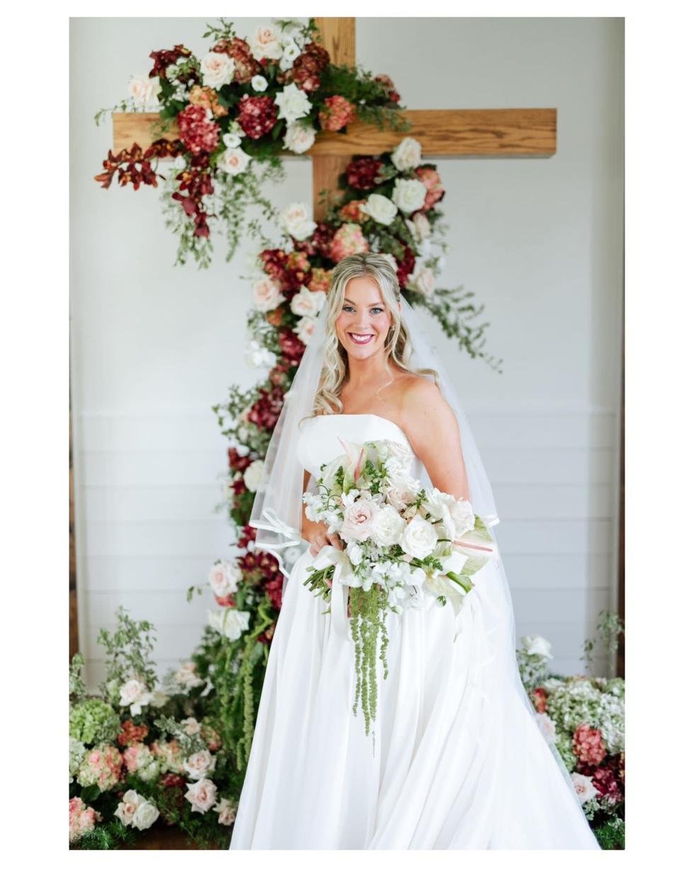 Bride beside a wooden cross with a full floral installation at Gateley Hill Gardens