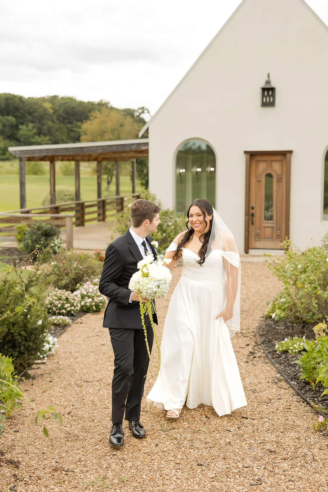 Jennifer and Hayden walking the garden path by the white chapel at Gateley Hill Gardens